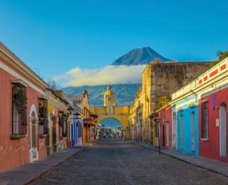 Stille gade med farverige huse i Antigua i Guatemala med udsigt til blå himmel og vulkan i baggrunden